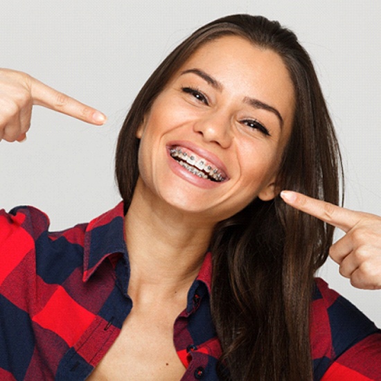 A young woman smiling and pointing to her braces after seeing an orthodontist in New Hampshire