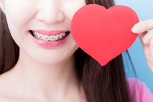 Woman with adult braces in Hudson holding paper heart and smiling